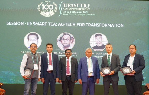 Group of six individuals at the UPASI TRF Centenary Conference, standing on stage, holding awards, with a backdrop displaying the event details and a theme about 'Smart Tea: Ag-Tech for Transformation'.